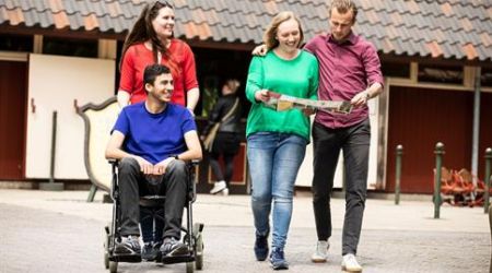 een groep mensen op pad met iemand in een rolstoel