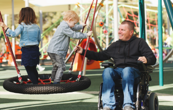 Vader in rolstoel met kind in een speeltuin