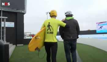 Ben loopt met zijn surfplank en begeleider naar het water toe