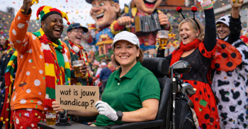 Een groep carnavalsvierders, waarvan een in een rolstoel met bordje 'Wat is jouw handicap?'