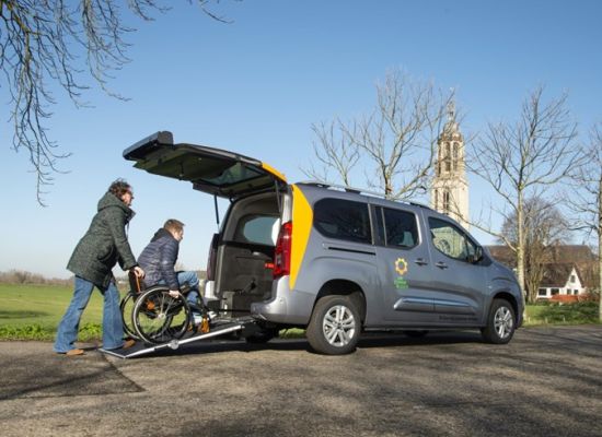 De Zonnebloemauto waar een persoon in een rolstoel door een kennis of familie via oprijplaten in de auto geduwd wordt