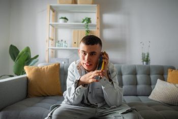 Jongeman is aan het bellen met zijn mobieltje, zittend op de bank in zijn woonkamer