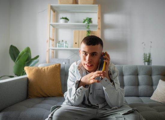 Jongeman is aan het bellen met zijn mobieltje, zittend op de bank in zijn woonkamer