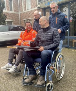 Twee personen in een rolstoel met achter zich twee personen om de rolstoel te duwer