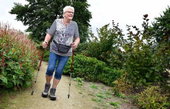 mevrouw met nordic walking stokken wandelt over een pad