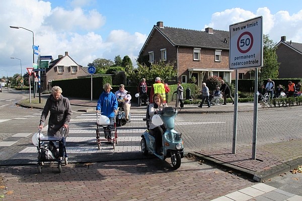 Gezelschap met rollators, rolstoelen, scootmobielen en blindenstokken bij obstakel zebrapad
