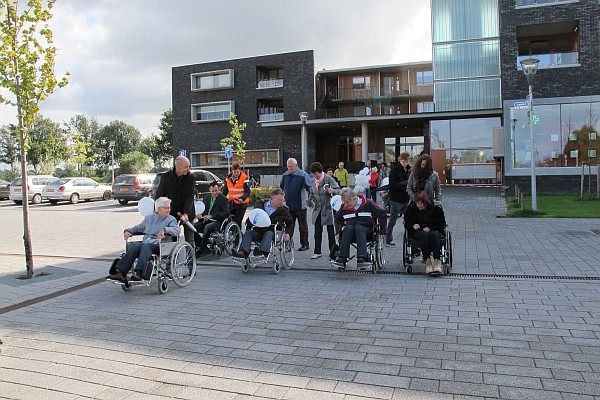 Gezelschap met rollators, scootmobielen, rolstoelen en blindenstokken voor obstakel goot bij Dolium