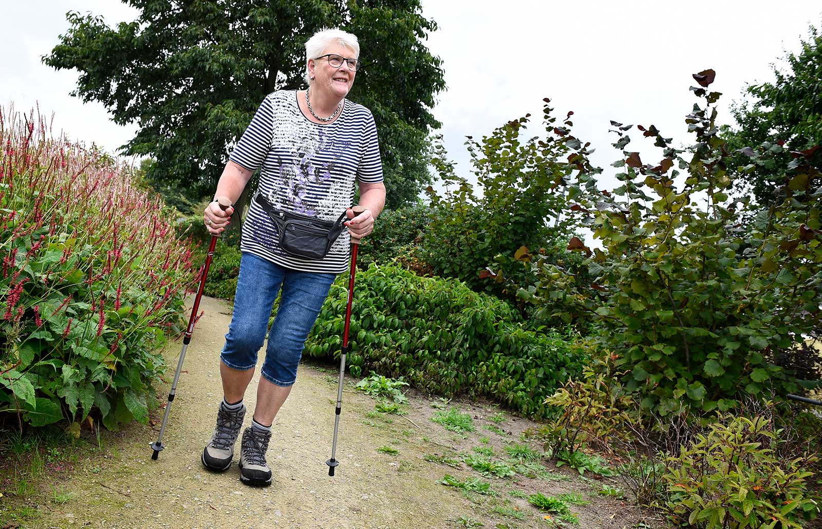 mevrouw met nordic walking stokken wandelt over een pad