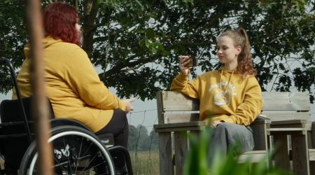 Twee jongeren in het park, een in een rolstoel, de andere zittend op een bankje