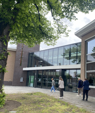 Medewerkers lopen met taststok en oogmaskers op voor de ingang van het gemeentehuis