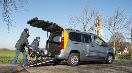 De Zonnebloemauto waar een persoon in een rolstoel door een kennis of familie via oprijplaten in de auto geduwd wordt