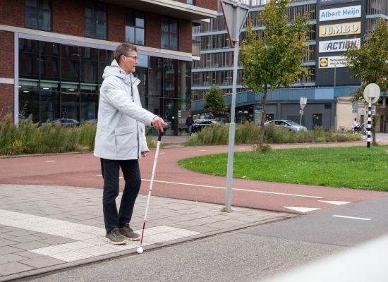Persoon met witte stok geeft aan dat hij wil oversteken