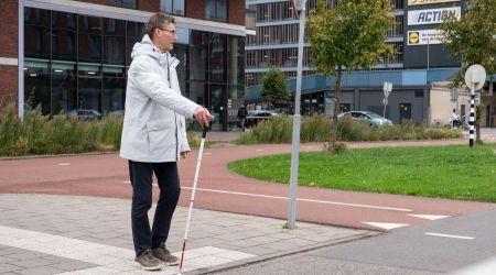 Persoon met witte stok geeft aan dat hij wil oversteken