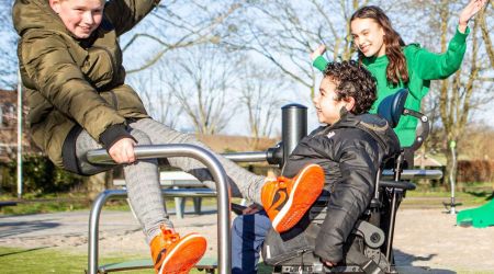 Drie kinderen, waarvan 1 in een rolstoel, spelen samen op een toegankelijk speeltoestel