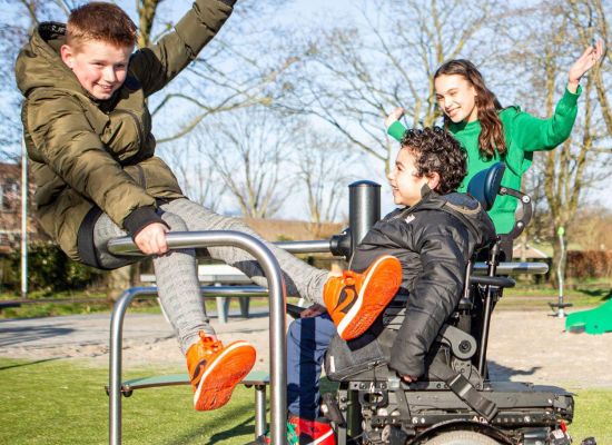 Drie kinderen, waarvan 1 in een rolstoel, spelen samen op een toegankelijk speeltoestel
