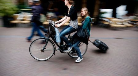 Twee jongedames op de fiets. Een achterop met een koffer op wieltjes