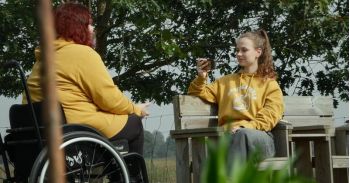 Twee jongeren in het park, een in een rolstoel, de andere zittend op een bankje