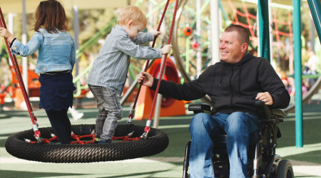 Vader in rolstoel met kind in een speeltuin
