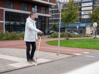 Persoon met witte stok geeft aan dat hij wil oversteken