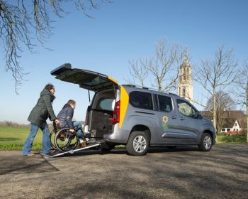 De Zonnebloemauto waar een persoon in een rolstoel door een kennis of familie via oprijplaten in de auto geduwd wordt